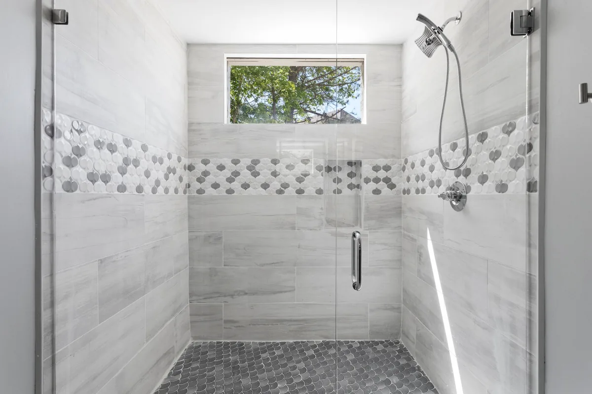 Glass-enclosed tiled residential shower with decorative mosaic band